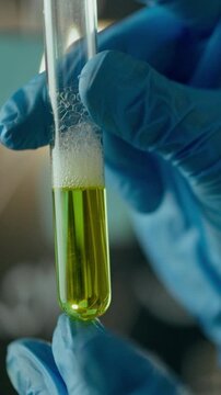 Woman chemist in well-lit office laboratory carefully grips glass test tube, observing the liquid sample with calibrated spectrometer and notes on blackboard, illustrating precise analytical routine
