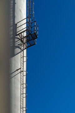 Industrial silo with metal ladder and platform reaching blue sky