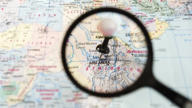 Hand-held magnifying glass focuses on Adis Abeba on paper map