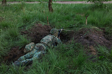 Obraz premium A soldier aims a service rifle from a prone fighting position in tall grass during a military exercise.