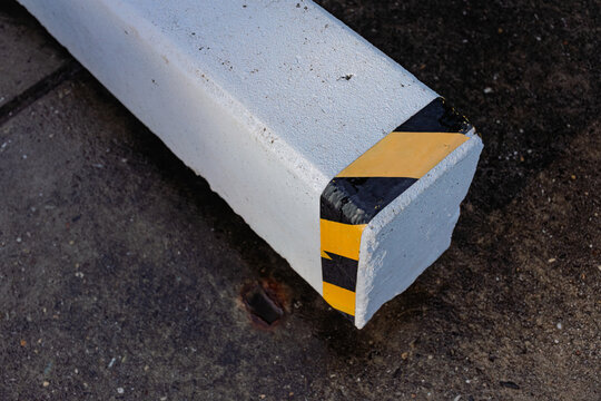A white concrete wheel stop with yellow and black hazard stripes lies on tarmac in a car park.