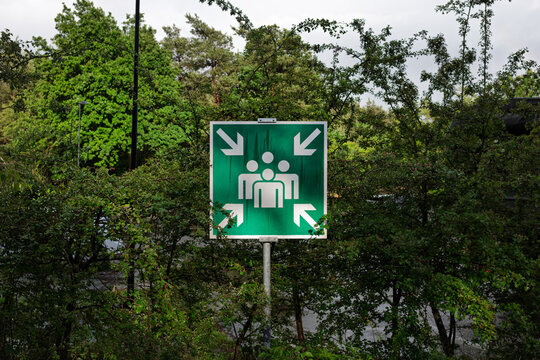 A green assembly point safety sign on a pole marks a muster area at a military training site.