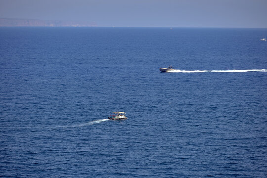 Motorboat and leisure pontoon boat cruising across the Mediterranean Sea off Magaluf, Mallorca, Balearic Islands, Spain, leaving white wakes on calm blue summer water.