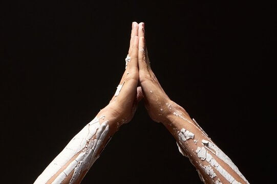 Hands in prayer pose covered with cracked white paint on a black background