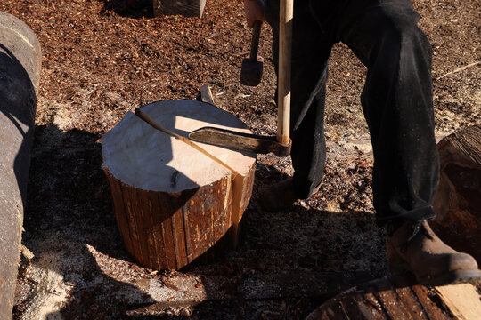 Forestry worker splitting a spruce log with a splitting maul and sledgehammer in a traditional timber yard