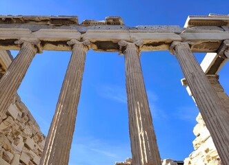Fototapeta premium Low-angle view of the Ionic columns of the Erechtheion on the Acropolis Hill in Athens, Greece, showcasing finely carved marble volutes and the ancient entablature rising against a summer blue sky.