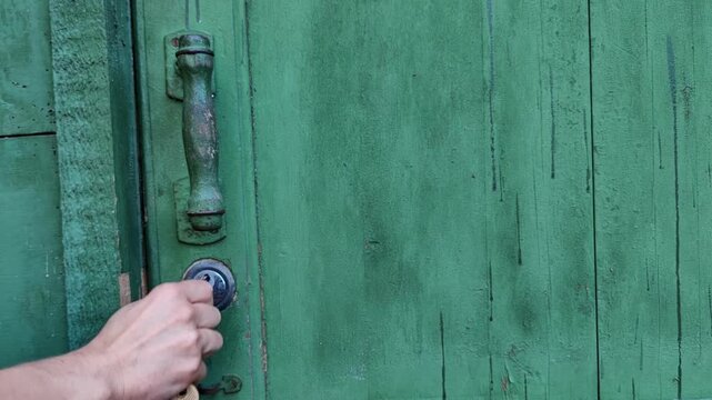 woman unlocks an old green wooden door using a key, home security, property access, rustic entrance, close up of lock mechanism.