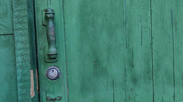 woman continues unlocking a weathered green wooden gate with a metal key, rustic locking system, property security, residential entrance.