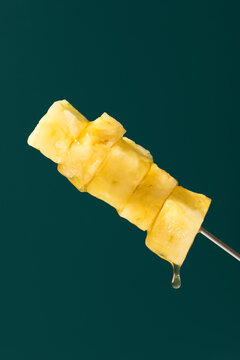 Fresh pineapple skewer with syrup drip on dark background