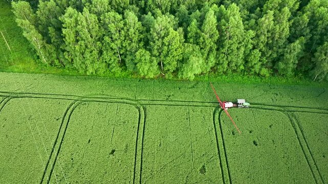 Aerial view of a crop duster spraying a field adjacent to a dense forest