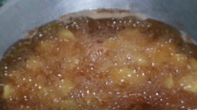 Potatoes frying in hot bubbling oil inside a metal cooking pan.