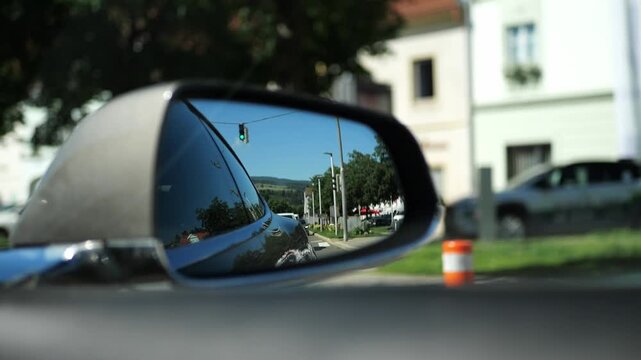 Side mirror reflecting a small-town street at a green traffic light in summer