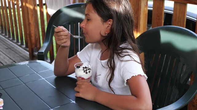 Girl eating a berry yogurt parfait at an outdoor patio table in summer