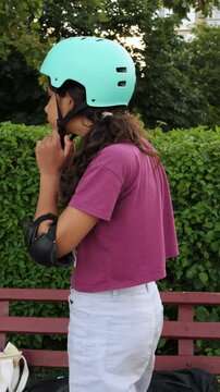Girl in skate helmet and elbow pads removing helmet in a summer park