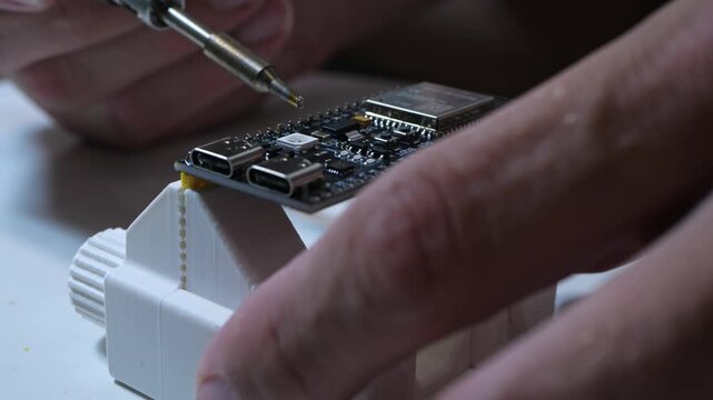 Hand probing a microcontroller circuit board with USB-C ports, close-up