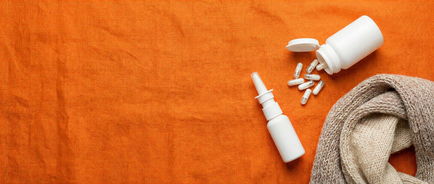 Nasal spray and capsules beside warm knitwear on orange background. Autumn cold and flu treatment concept with copy space