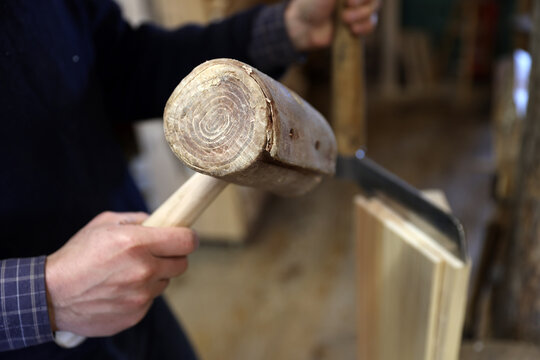 Craftsman using a wooden mallet and a traditional froe to split spruce wood for handcrafted tavaillons in the Haut-Jura, France