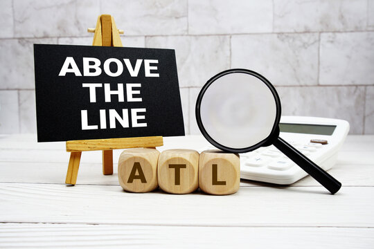 ATL Above The Line text with calculator magnifying glass and on wooden background