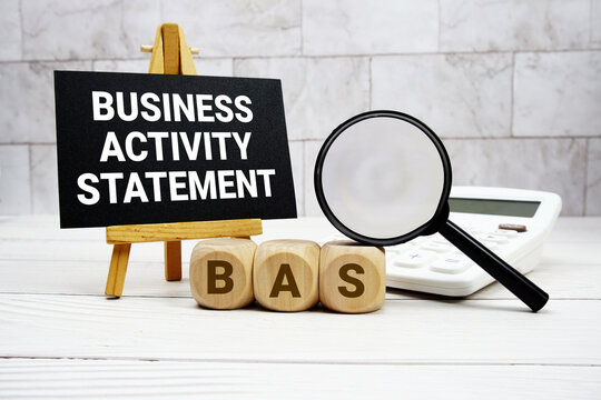 BAS Business Activity Statement text with calculator magnifying glass and on wooden background