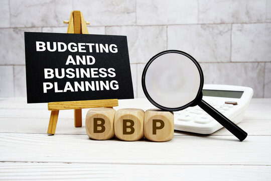 BBP Budgeting and Business Planning text with calculator magnifying glass and on wooden background