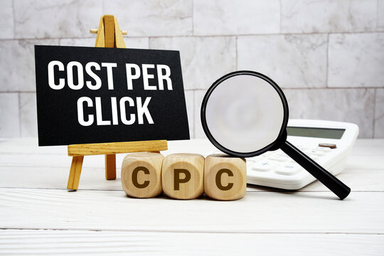 CPC Cost Per Click text with calculator magnifying glass and on wooden background