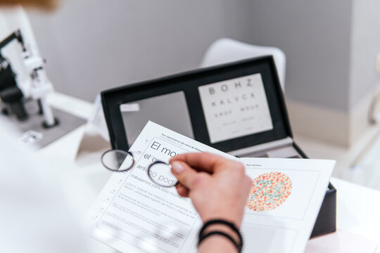 Woman examine eye chart with magnifying glass in optician office