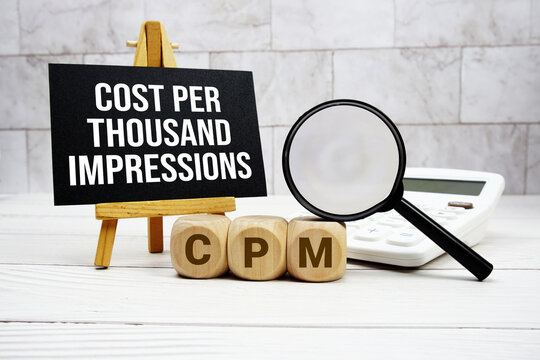 CPM Cost Per Thousand Impressions text with calculator magnifying glass and on wooden background