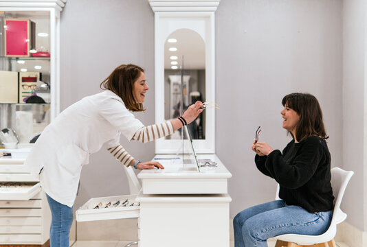 Optician help woman choose eyeglass frame in optical store