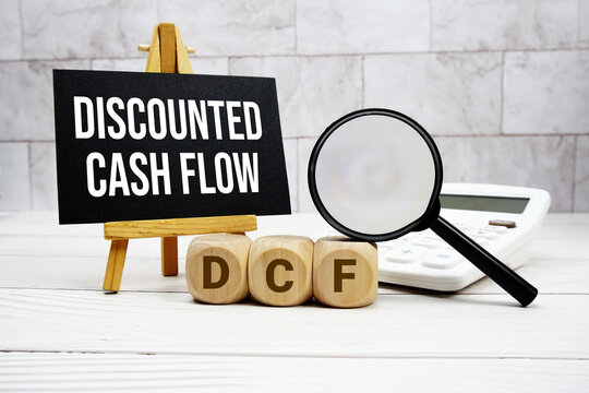 DCF Discounted Cash Flow text with calculator magnifying glass and on wooden background
