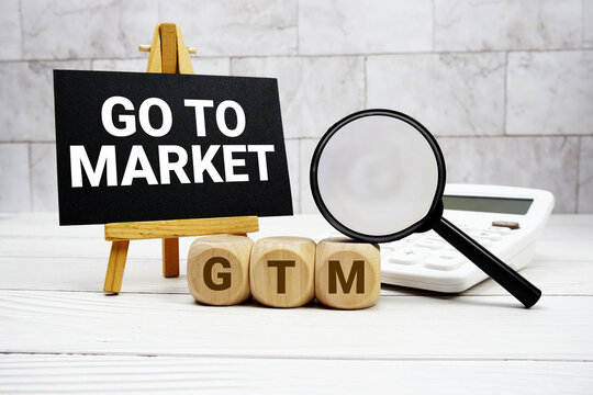 GTM Go To Market text with calculator magnifying glass and on wooden background