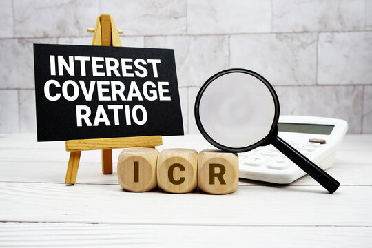 ICR Interest Coverage Ratio text with calculator magnifying glass and on wooden background