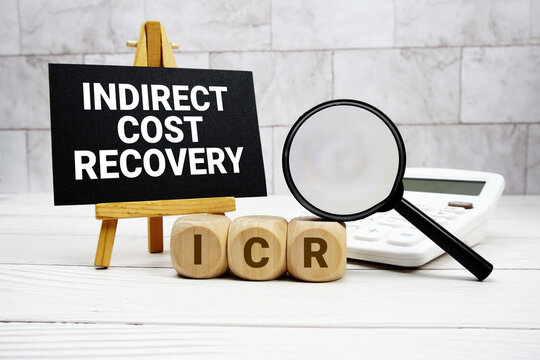 ICR Indirect Cost Recovery text with calculator magnifying glass and on wooden background