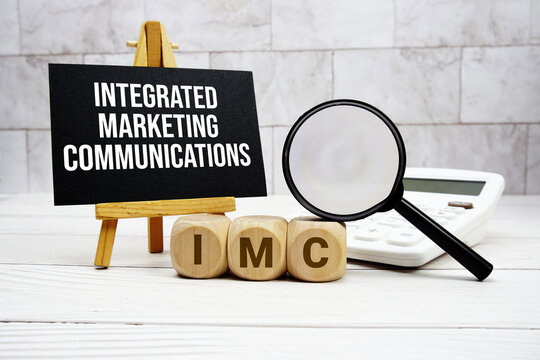 IMC Integrated Marketing Communications text with calculator magnifying glass and on wooden background