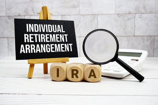 IRA Individual Retirement Arrangement text with calculator magnifying glass and on wooden background