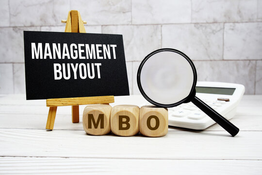 MBO Management Buyout text with calculator magnifying glass and on wooden background