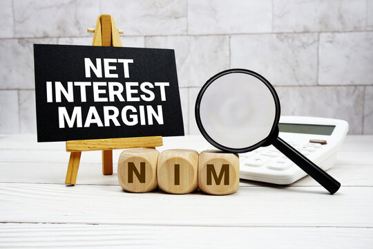 NIM Net Interest Margin text with calculator magnifying glass and on wooden background