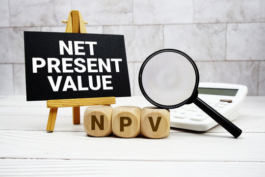 NPV Net Present Value text with calculator magnifying glass and on wooden background