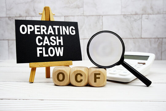 OCF Operating Cash Flow text with calculator magnifying glass and on wooden background
