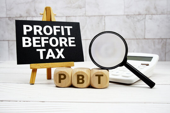 PBT Profit Before Tax text with calculator magnifying glass and on wooden background