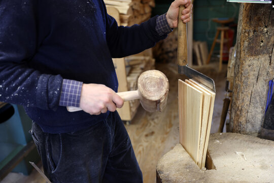 Craftsman splitting spruce wood with a froe and wooden mallet to produce traditional tavaillons in the Haut-Jura, France