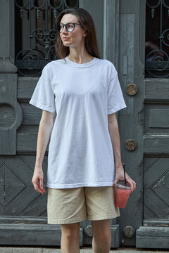 Woman in white t-shirt and shorts holding a pink drink outside a vintage door