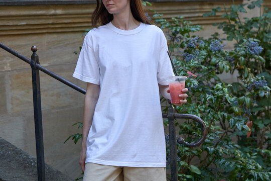 Woman in white t-shirt holding a pink drink outdoors near greenery