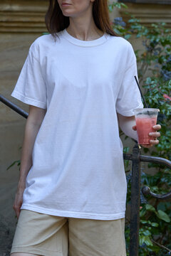 Woman in white t-shirt and shorts holding a refreshing pink drink outdoors