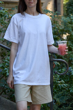 Woman in white t-shirt and shorts holding a refreshing pink drink outdoors