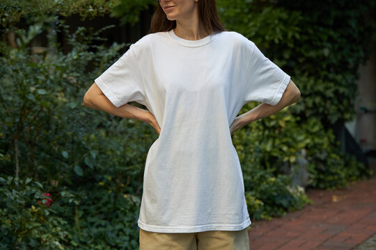Woman wearing a plain white t-shirt and tan shorts outdoors with green foliage