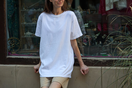 Woman wearing a plain white t-shirt and beige shorts leaning against a wall