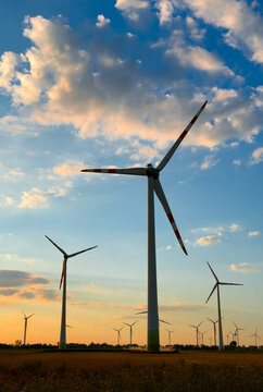 Sunset wind turbines in nature. Wind turbines stand tall in a field during sunset. The sky shows colorful clouds and soft light as day ends.