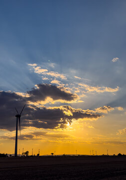 Sunset behind wind turbine in open field. A wind turbine stands in an open field as the sun sets behind clouds, creating a colorful sky at evening time.