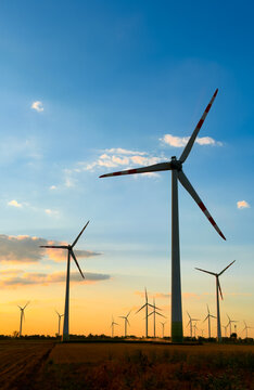 Wind turbines stand in a field at sunset. Wind turbines turn in the evening light as the sun sets in the background, creating a scenic view in the countryside.