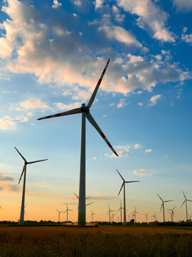 Wind turbines produce field energy. Wind turbines stand in a field during sunset. The sky shows clouds and a mix of colors above the rural landscape.